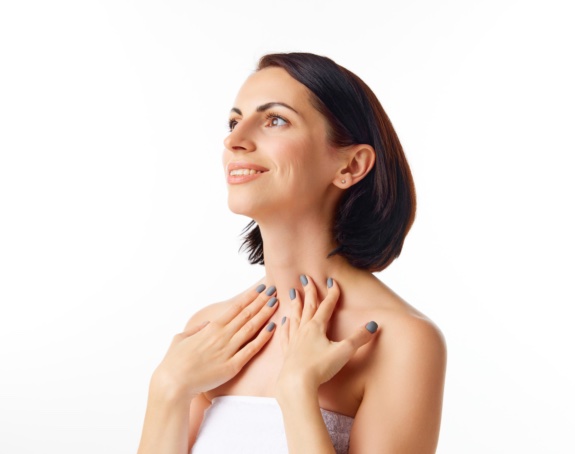 Side view portrait of smiling, pretty woman with brunette hair doing neck hand massage over white studio background. Beauty, spa, cosmetology, skin care, emotion concept. Model with well-kept skin